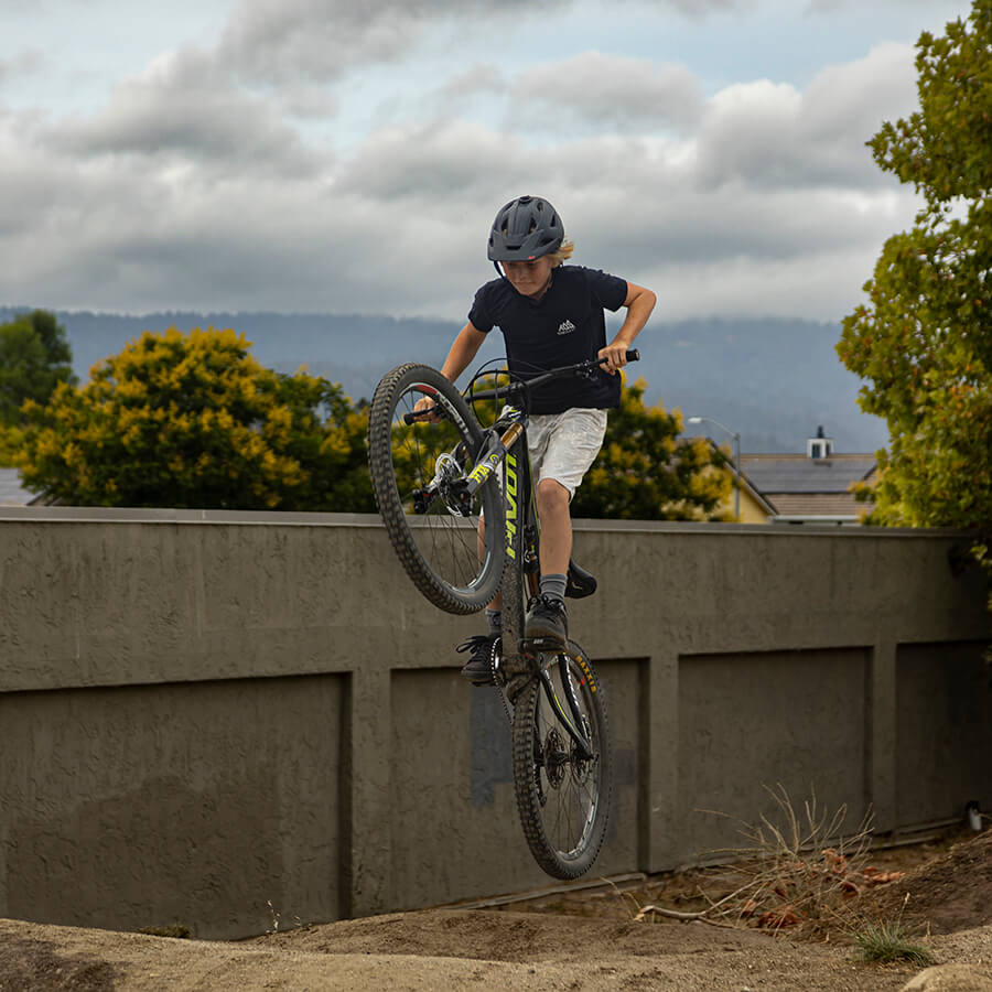 Young teenager jumping off a lip at a pump track wearing TOS Premium Youth shirt. in black. 