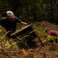 Male wearing brown tan brown trucker hat with TOS classic logo. Digging with a friend in the forest. 